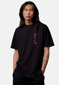 Schwarzes T-Shirt mit kurzen Ärmeln und Rundhalsausschnitt, mit rotem grafikschriftzug auf der Brust und lässigem Schnitt. Glatte Stofftextur.