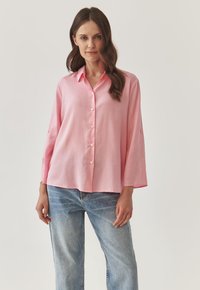 Lichtroze, lange mouwen shirt met een knoopsluiting aan de voorkant, comfortabele pasvorm en zachte textuur. Gecombineerd met blauwe denim jeans.