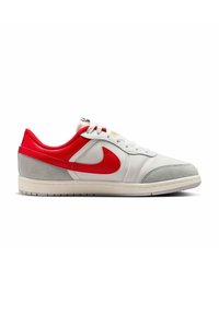 Χαμηλό sneaker με λευκό διχτυωτό υλικό, γκρι σουέτ τοκά, κόκκινο γιακά, κόκκινο σήμα Nike και λευκή σόλα σε λευκό φόντο.