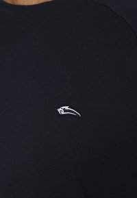 Marinblå t-shirt med kort ärm i mjukt tyg, med en liten vit broderad logotyp på vänster bröstområde. Rundad halsringning.