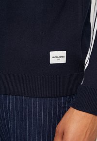 Marineblaues Sweatshirt aus strukturiertem Strickstoff, mit gerippten Bündchen und Saum, ausgestattet mit einem weißen Etikett mit "JACK&JONES CORE" an der Unterseite.