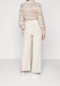 Pantaloni ampi a coste di un beige chiaro abbinati a un maglione corto lavorato a maglia multicolore con strisce pastello. Texture liscia e vestibilità comoda.