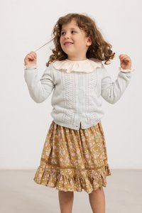 Cardigan a maglia grigio chiaro con un motivo testurizzato, abbinato a una gonna floreale marrone con orlo a volant e dettagli in pizzo.