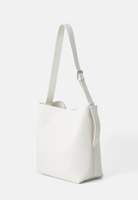Valkoinen rei'itetty käsilaukku neliömäisessä muodossa, säädettävällä olkahihnalla ja sileällä tekstuurilla. Ominaisuuksena minimalistic muotoilu.