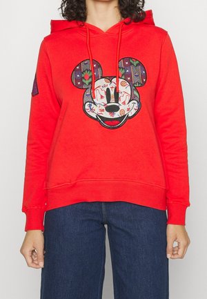 Rød hættetrøje med et farverigt mønstret Mickey Mouse-ansigt på fronten, båret med mørkeblå jeans.