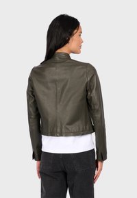 Smaragdově zelená kožená bunda s přiléhavým střihem, zkrácenou délkou a vysokým límcem. Materiál vypadá hladce s minimem švů.