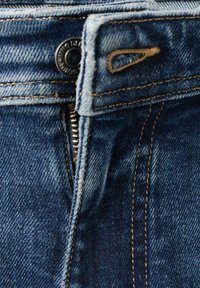 Jeans in denim blu con chiusura a zip, dettagli in rame e cuciture a contrasto. Il tessuto presenta una finitura strutturata con scoloriture.