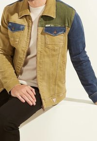 Kleurblok denimjack met groene, gele en blauwe panelen, twee borstzakken, merklabel en een gestructureerde afwerking.