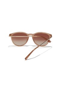 Occhiali da sole rosa chiaro con design rotondo, lenti marroni sfumate, montatura trasparente e aste metalliche sottili. Dettagli minimalisti in tutto.