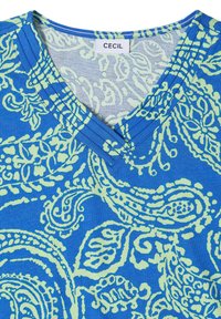 Chemise bleue à col en V avec des motifs cachemire vert clair et une étiquette blanche avec le nom de la marque "Cecil" à l'intérieur du col.