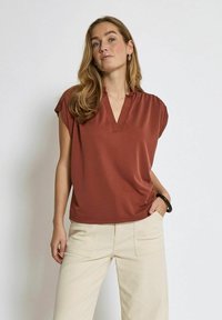 Top corto color ruggine con scollatura a V e vestibilità rilassata, abbinato a pantaloni a gamba larga color crema. Tessuto liscio e leggero.