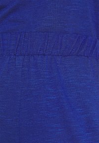 Blå atletisk tyg med en texturerad yta, elastisk midja med gathered-detaljer och en jämn övergripande utseende.