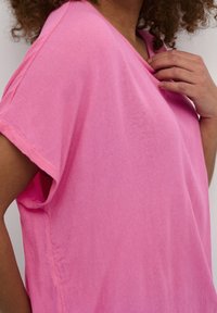 Lyserød, løstsiddende t-shirt i letvægtsstof med korte ærmer og afslappet udskæring, der viser en blød struktur og et afslappet design.