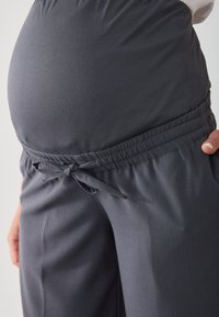 Tehotenské nohavice z tmavosivej látky s elastickým pásom a viazaním, s voľným strihom, ktorý sa prispôsobuje rastúcemu bruchu.