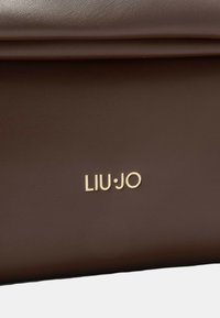 Hnědá kožená kabelka s hladkým povrchem, na přední straně s zlatým logem "LIU·JO". Skládaný design s čistými liniemi.