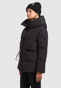 Must have puffer jakk must kõrge krae, lukuga sulgemine, külgkinni ja logopatch varrukal. Materjal näeb välja sile ja soojustatud.
