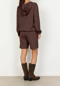 Bruine hoodie met een relaxte pasvorm, gecombineerd met bijpassende shorts. De outfit heeft ribgebreide manchetten en gestructureerde bruinleren kniehoge laarzen.