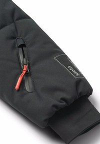 Manica di giacca trapuntata nera con tasca laterale dotata di una cerniera nera e di un tirante rosso. Etichetta con "nolo" stampata su un pannello decorativo.