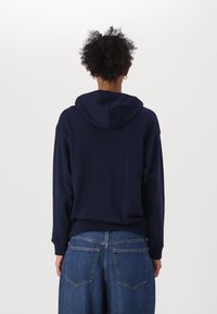 Marinblå hoodie med dragsko i huvan, långa ärmar och en avslappnad passform, tillsammans med högmidjade blå jeans.