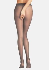 Nieprzezroczyste brązowe rajstopy o delikatnej fakturze, z wysokim stanem i wzmocnionymi palcami, pokazane od tyłu, z ręką opartą na biodrze.