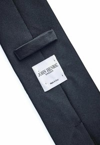 Mörkgrått tygband med diagonalt ribbat mönster. Har en vit etikett som säger "JOHN HENRIC SWEDEN" och "Tillverkad i Italien."