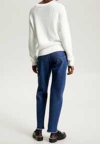 Witte gebreide trui met een gestructureerd patroon, gecombineerd met aansluitende blauwe jeans met een ruwe zoom. De outfit wordt compleet gemaakt met zwarte schoenen.