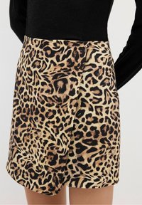 Mini-jupe à imprimé léopard avec un design ceinturé, fabriquée en tissu doux avec un schéma de couleurs beige et noir et des motifs de texture visibles.