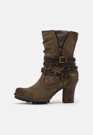 Bota marrón hasta la mitad de la pantorrilla con tacón, dos correas decorativas con hebillas, detalle de cadena, cremallera frontal y panel de tela texturizada en la parte superior.