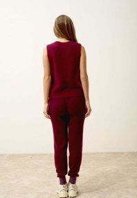 Burgundy ärmlös stickad topp som matchas med joggers. Mjuk textur, figurnära form och uppvikta byxor. Vita sneakers fulländar looken.