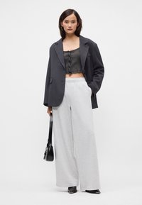 Γκρίζα oversized σακάκι, ριγέ μαύρο crop top, φαρδιά γκρίζα φόρμα και μαύρη τσάντα. Απαλή ύφανση, χαλαρή εφαρμογή, casual σχέδιο, ελάχιστες λεπτομέρειες.