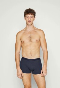 Mørkeblå bomullsboxershorts med mykt elastisk midjebånd, som har en tettsittende passform og minimal søm for komfort. Modellen står oppreist mot en enkel bakgrunn.