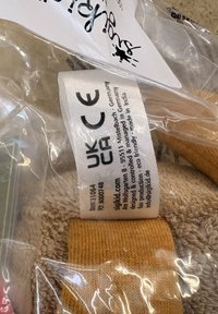 L'étiquette de vêtement à l'intérieur d'une pochette en plastique transparente affiche les marques CE et UKCA, le nom de la marque sigikid, ainsi que les informations sur le produit, y compris l'origine et la conception écologique.