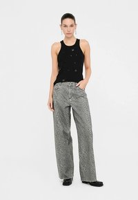 Black sleeveless top with embellishments paired with gray wide-leg pants featuring a geometric pattern and frayed hem. Black shoes complete the outfit.