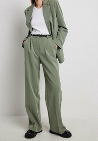 Ljusgrön, strukturerad kostym med avslappnade byxor och skräddarsydd kavaj, i kombination med en vit skjorta och svarta plattformsskor. Standard passform.