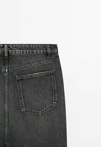 Vue arrière d'un jean en denim noir montrant la ceinture avec passants pour ceinture et une poche arrière unique avec des coutures visibles.
