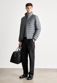 Pelēks pūkains jaka ar horizontālām pārplūdes līnijām, augstu apkakli, rāvējslēdzēju, apvienota ar melniem korduroja biksēm un melnu sporta maisiņu. Melni apavi.