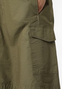 Oliven grøn nederdel med tekstureret overflade, der har en sidelomme og et enkelt, lige design. Fremstillet af letvægtsmateriale.