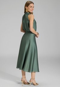 Robe en satin verte avec un design sans manches, taille cintrée et jupe évasée, dotée d'un col haut et d'un détail de dos en trou de clé.