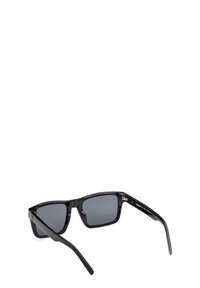 Occhiali da sole in plastica nera con lenti grigie, forma rettangolare, stanghette dritte e branding discreto sulla montatura interna. Texture liscia.