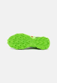 Semelle en caoutchouc verte avec une surface texturée dotée de crampons de traction proéminents et d'une accent rouge. Le design est audacieux et fonctionnel.