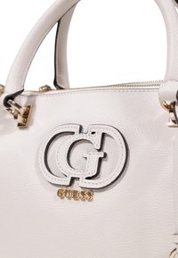 Borsa a tracolla bianca con texture, caratterizzata da un evidente logo duale intagliato, dettagli in metallo dorato e chiusura a zip. Le maniglie sono strutturate per una presa sicura.