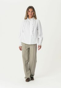 White long-sleeve blouse with ruffled collar and cuffs, paired with beige wide-leg trousers. Blouse features button closure and soft fabric.