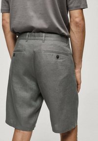 Shorts en lin gris avec une coupe décontractée, dotés de deux poches arrière avec des fermetures à bouton unique et des passants de ceinture, montrés sous un angle arrière.