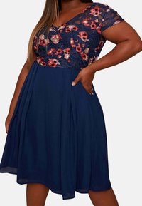 Námořnické šaty s květinovou v ýšivkou, výstřihem do V a krátkými krajkovými rukávy. Mají rozšířený pas a kapsy pro větší pohodlí.