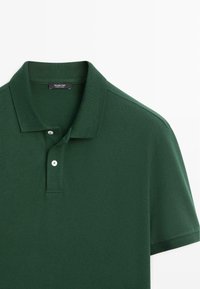 Polo à manches courtes vert foncé avec deux boutons blancs et un col classique, posé à plat sur un fond blanc.