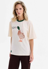 Krémové tričko se zeleným žebrovaným límečkem, na kterém je grafika kachny divoké a nápis "JUPÍ, JE VÍKEND." Krátké rukávy.