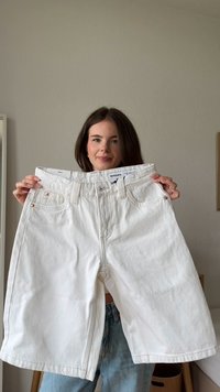 Valkoiset farkkushortsit väljällä istuvuudella, joissa on perinteinen viiden taskun malli, metalliset yksityiskohdat_TASKUISSA ja leveä lahje.