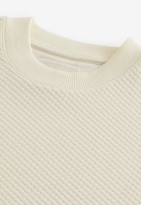 Felpa color crema con un design a coste trapuntato e colletto a coste. Il tessuto morbido crea un aspetto liscio.