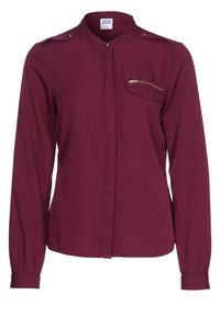 Blusa bordeaux a maniche lunghe con colletto alto, tasca con zip frontale, dettagli con bottoni sulle spalle e polsini abbottonati. Realizzata in tessuto leggero.
