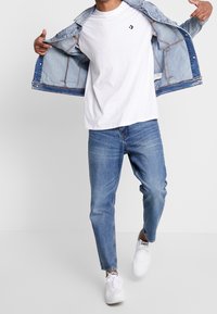 Vit t-shirt, ljusblå denimjacka och ljusblå jeans. Vita sneakers med svarta accenter. Avslappnad outfit visad.